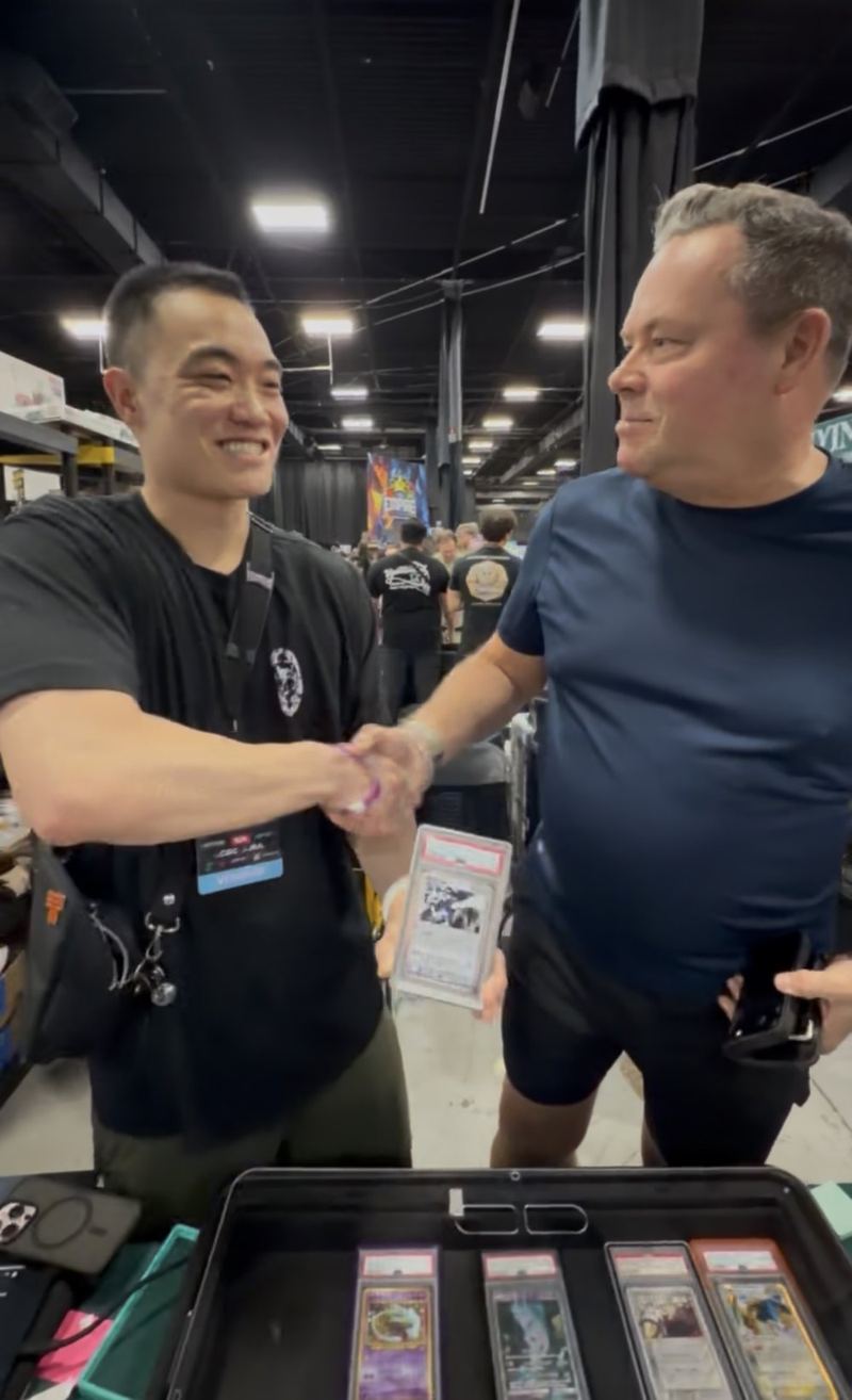 Two collectors shaking hands over a graded card and a case of slabs.
