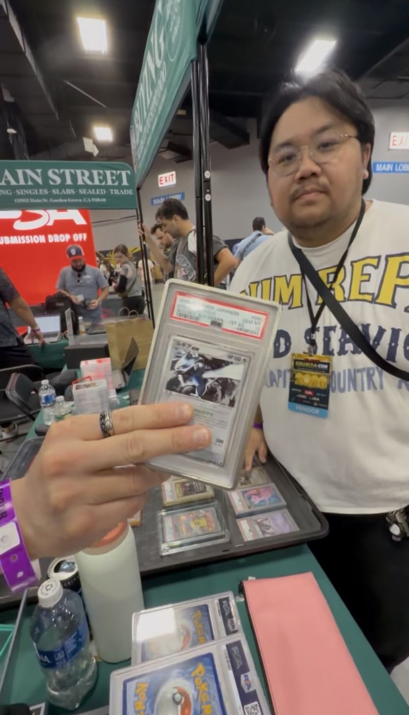 A vendor showing a graded Japanese Pokémon card across a table of slabs.